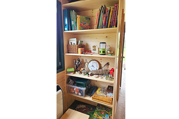 Schutzwagen der Naturkita Appen 2 Helles Holzregal mit Büchern und Sammelstücken aus der Natur im Schutzwagen der Naturkita Appen